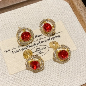 Primer plano de pendientes redondos vintage con cristal rojo y pavé dorado.