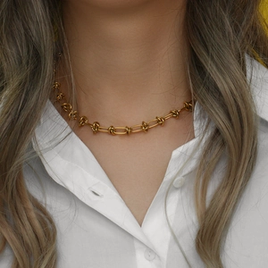 Detailed view of a gold knot chain necklace worn by a model in a white shirt