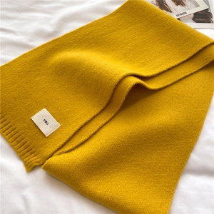 Detail of bright yellow knitted scarf with soft texture and white branded woven label