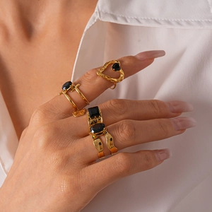 Détail de trois bagues dorées superposées ornées de zircons noirs à facettes élégants