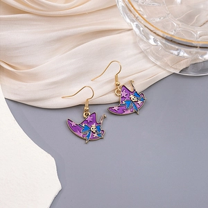 Detail of purple witch hat earrings with blue bows and gold skull accents on silk