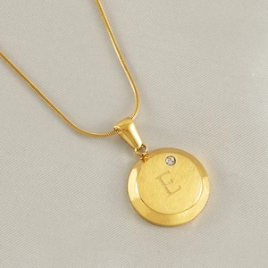 Macro detail of gold 18K letter E pendant with small diamond on snake chain