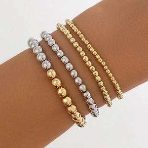 Close-up of stacked gold and silver beaded bracelets with heart pendants on wrist