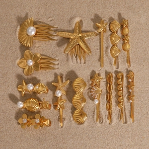 Golden sea shell and starfish hair pins with pearls on sand for a summer beach look