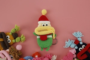 Detail of handmade green monster key case with red hat and yellow scarf crochet knit