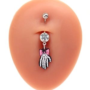 Macro shot of a belly ring featuring a skull hand pendant with a pink bow on silicone model