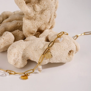 Gold chain necklace with shell and pearl charms on textured coral stone display