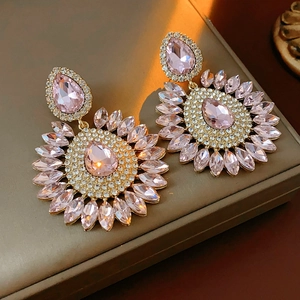 Close-up of golden teardrop earrings featuring pink crystal petals and a halo of small gems