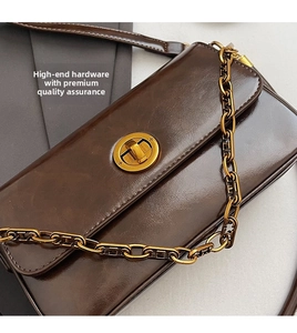 Close-up of golden round twist lock and thick chain on vintage brown leather handbag