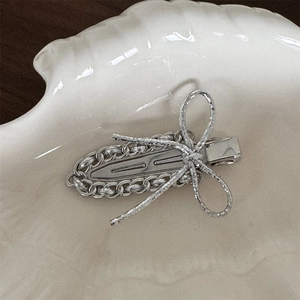 Detailed close-up of a silver bow hair clip with metal chain texture on a white shell tray