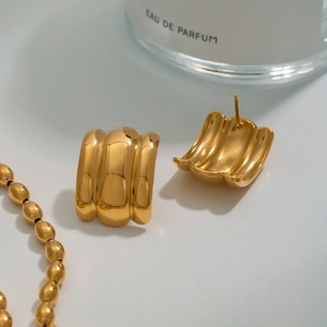 Polished gold thick stud earrings with ripple texture and beaded necklace shown on perfume bottle