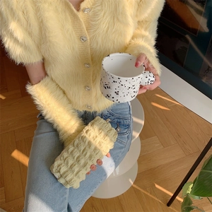 Close-up of yellow pleated stationery bag held by model wearing a fuzzy cardigan