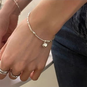 Detail shot of a silver heart charm bracelet paired with a sleek matching metal ring