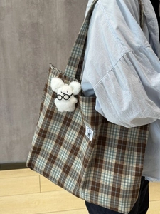 Detail view of plaid mini bag with white plush bear charm on a shoulder strap