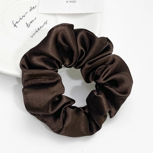 Detailed view of dark brown satin hair scrunchie with a glossy silk texture on a white plate
