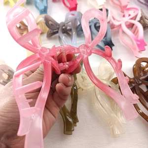 Translucent pink bow hair claw clip made of resin shown held in hand, 13cm size