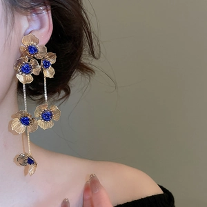 Detail of long gold tassel earrings featuring blue roses and hollow floral design