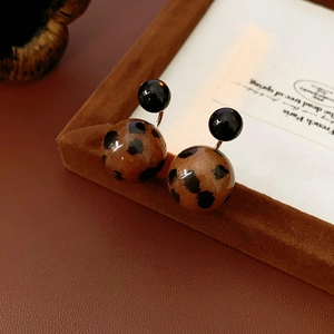 Detail of leopard print ball earrings with black top sphere inside a brown photo frame