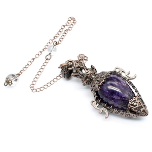 Close-up of antique copper hollow pendant with purple teardrop crystal and metal chain