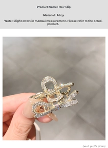 Detailed close-up of golden alloy hair claw clip with sparkling rhinestone wave design