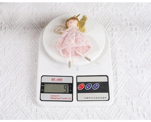 Détail d'un ange en dentelle rose de 9g avec des ailes dorées sur une balance numérique