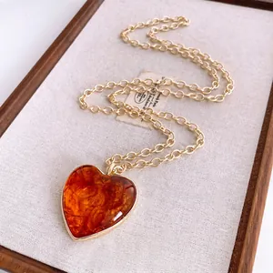 Maillard heart amber pendant necklace with chunky gold chain on white linen board