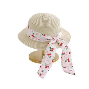 Kids flat top straw hat with cherry print ribbon and bow on a golden display stand