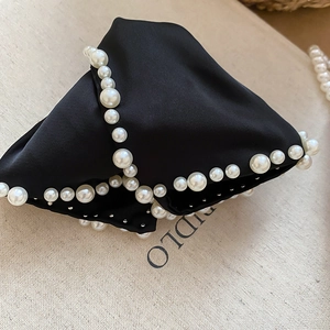 Détail d'un serre-tête en satin noir avec de grandes perles blanches et des clous argentés