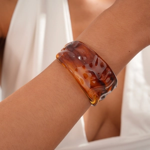 Macro shot of a chunky amber resin bangle with artistic irregular wave textures on skin