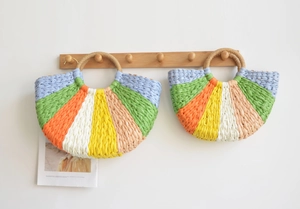 Detail of colorful striped handmade straw handbags hanging on wooden hooks against white wall