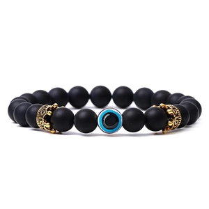 Detail of matte black beads with a blue evil eye and golden crowns on an elastic bracelet