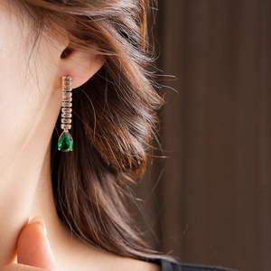 Close-up of a drop earring with emerald green waterdrop gem and rectangle zircons