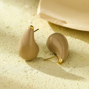 Close-up of khaki water-drop earrings on a textured stone base with gold accents