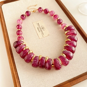 Détail de perles en résine magenta marbrée et entretoises dorées sur collier vintage