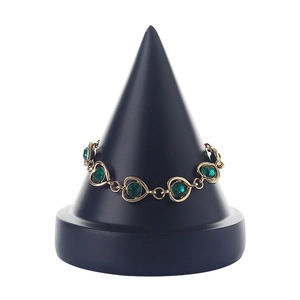 Golden bracelet with heart links and green gemstones on a black cone display stand