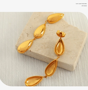 Detailed view of elegant gold-toned triple-drop earrings on a textured stone surface