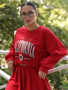 Dettaglio felpa rossa con stampa California e gonna sportiva su modella all'aperto