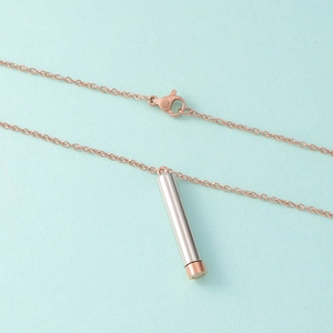 Detail of rose gold chain necklace with a telescopic silver cylinder pendant on blue