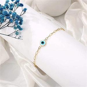Close-up of gold paperclip chain bracelet with a blue evil eye charm on silk background