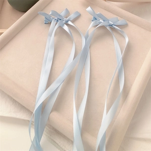 Detail view of two light blue satin bow hair clips with long ribbons on a soft tray