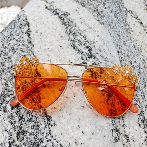 Detail view of gold pilot frame sunglasses with daisy accents and bright orange lenses