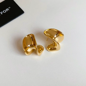 Close-up of gold-plated C-shaped earrings with irregular twisted organic metal design