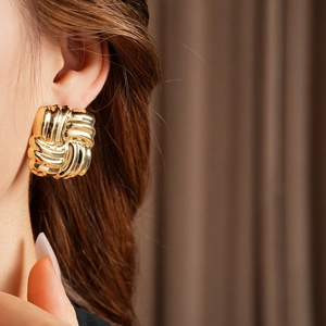 Close-up of gold square earrings with ripple texture worn by a model in natural lighting