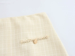 Détail du tissu en tweed beige avec bouton doré et franges tissées sur le rabat de poche