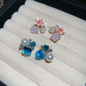 Macro shot of pink enamel flower and blue crystal stud earrings in a velvet box