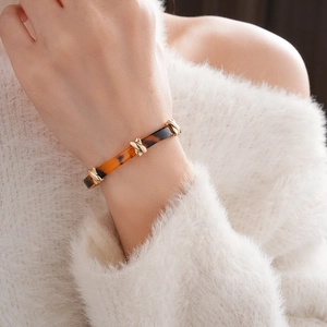 Close-up of leopard resin bangle with gold crisscross metal details on a white sweater