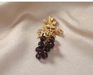 Detailed view of grape brooch with purple beads and gold leaves on champagne silk fabric