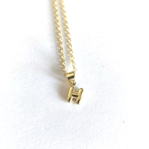 Detailed shot of a minimalist gold letter H pendant necklace with a polished finish