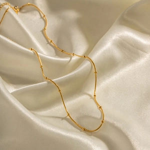 Detailed view of a gold snake chain necklace with beads on soft cream silk fabric