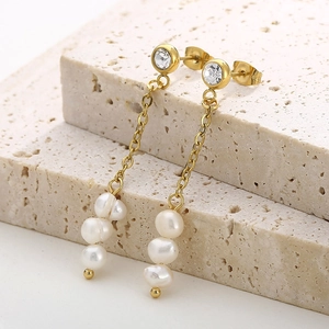 Détail macro de boucles d'oreilles pendantes en perles et or 18k sur pierre beige